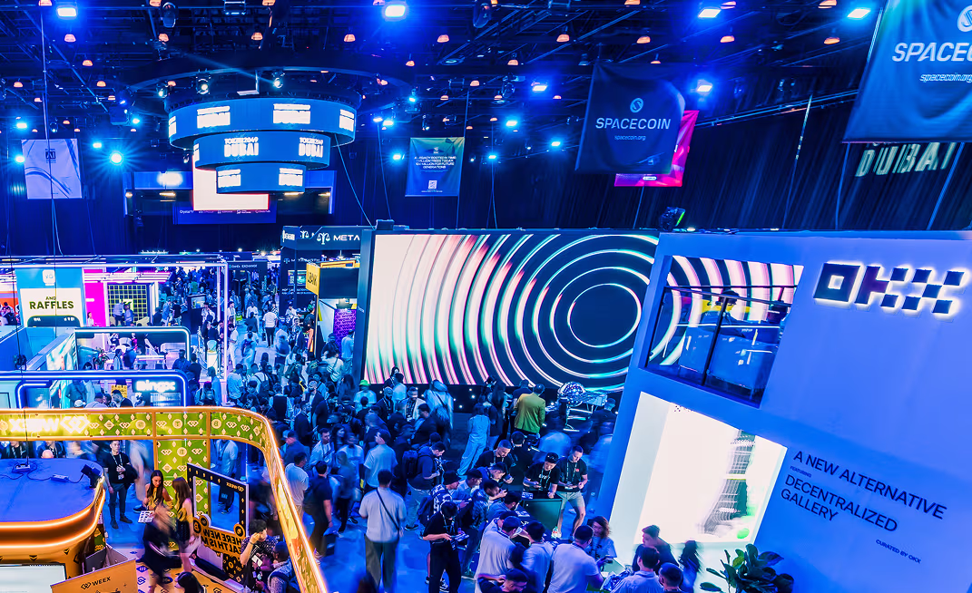 Large crowd attending a brightly lit technology expo with various booths displaying digital and blockchain themes, including SpaceCoin and OKX.